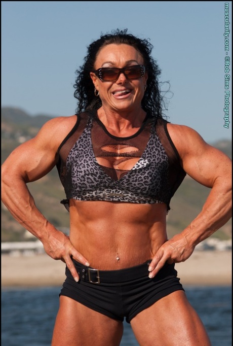 Brunette bodybuilder Sharon Mould poses on a beach while wearing sunglasses 30882760